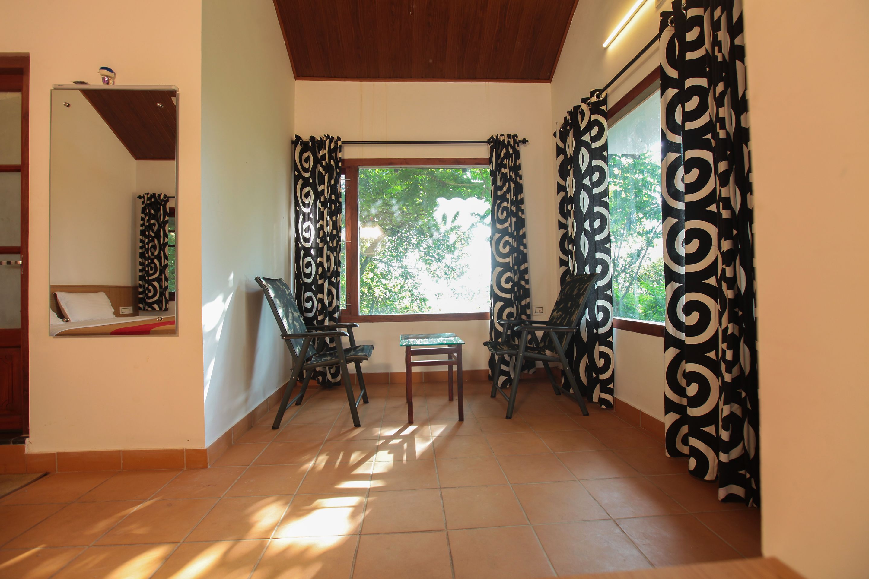 Una habitación con piso de baldosas, una ventana con cortinas, una mesita y dos sillas.