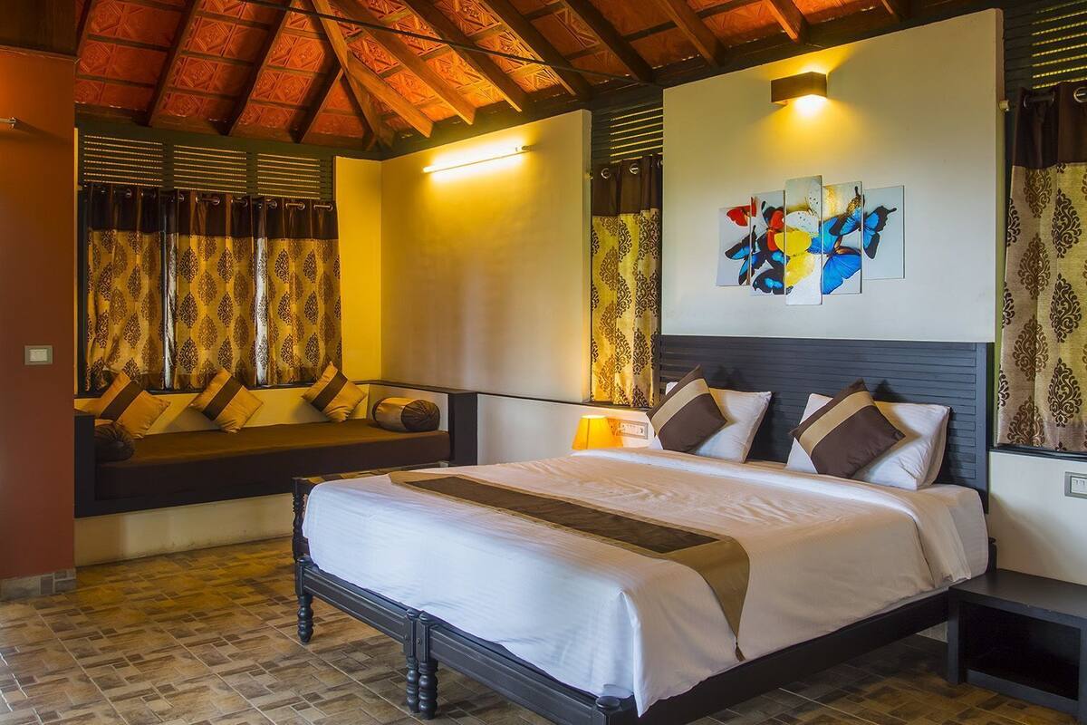 A bedroom with a bed, bedside tables, a headboard, a window with curtains, and a wall-mounted artwork.