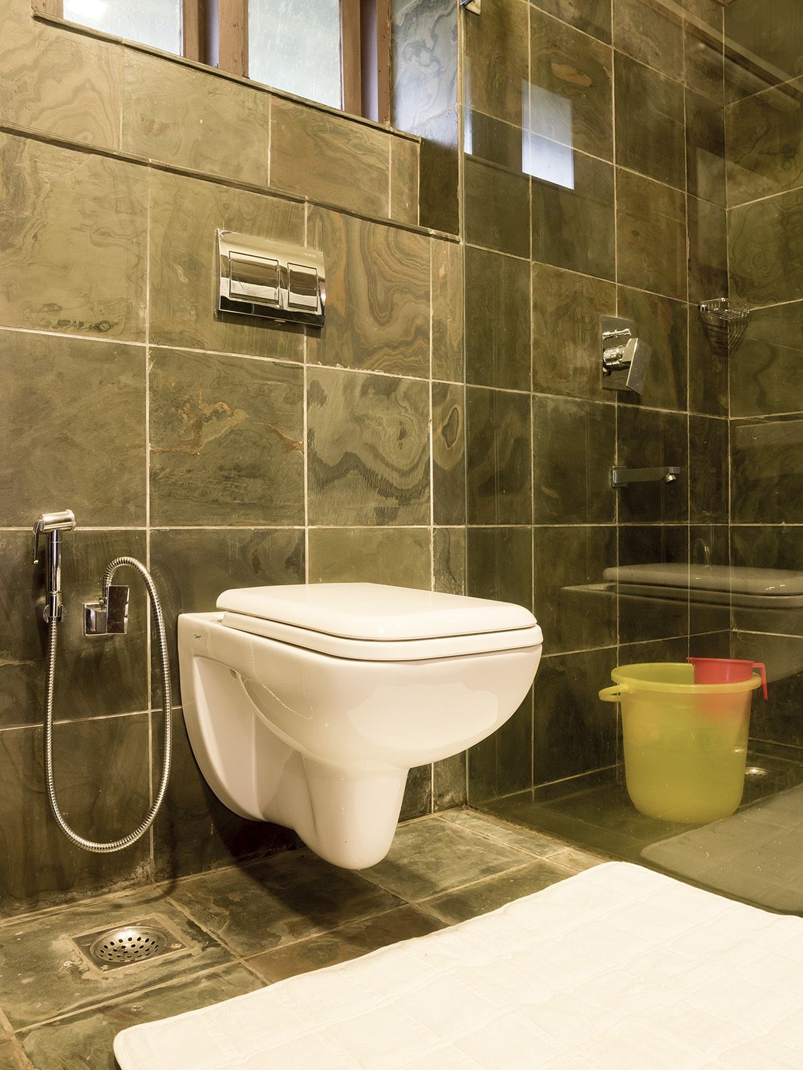 Un bagno con il water bianco, una doccia e un secchio giallo.