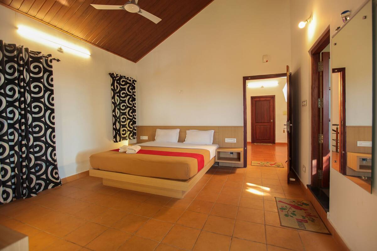 A hotel room with a bed, bedside tables, a ceiling fan, a mirror, and a door leading to another room.