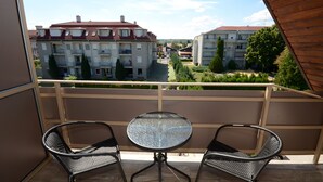 Un balcón con dos sillas de mimbre y una mesa de vidrio, con vista a un patio con edificios y árboles.