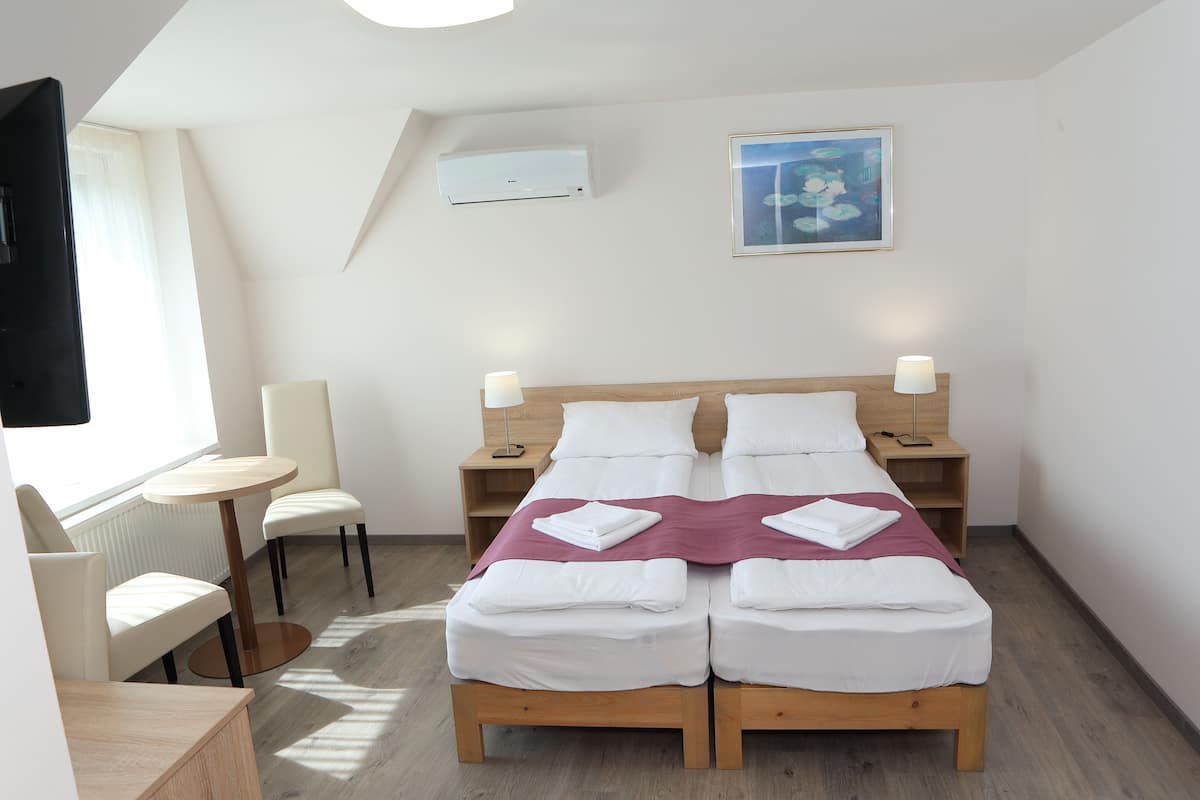 Quarto de hotel com uma cama de casal, duas mesas de cabeceira, uma cadeira, uma mesinha e uma televisão.