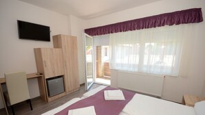 Un dormitorio con cama, escritorio, televisor y puerta corrediza de vidrio a un balcón.