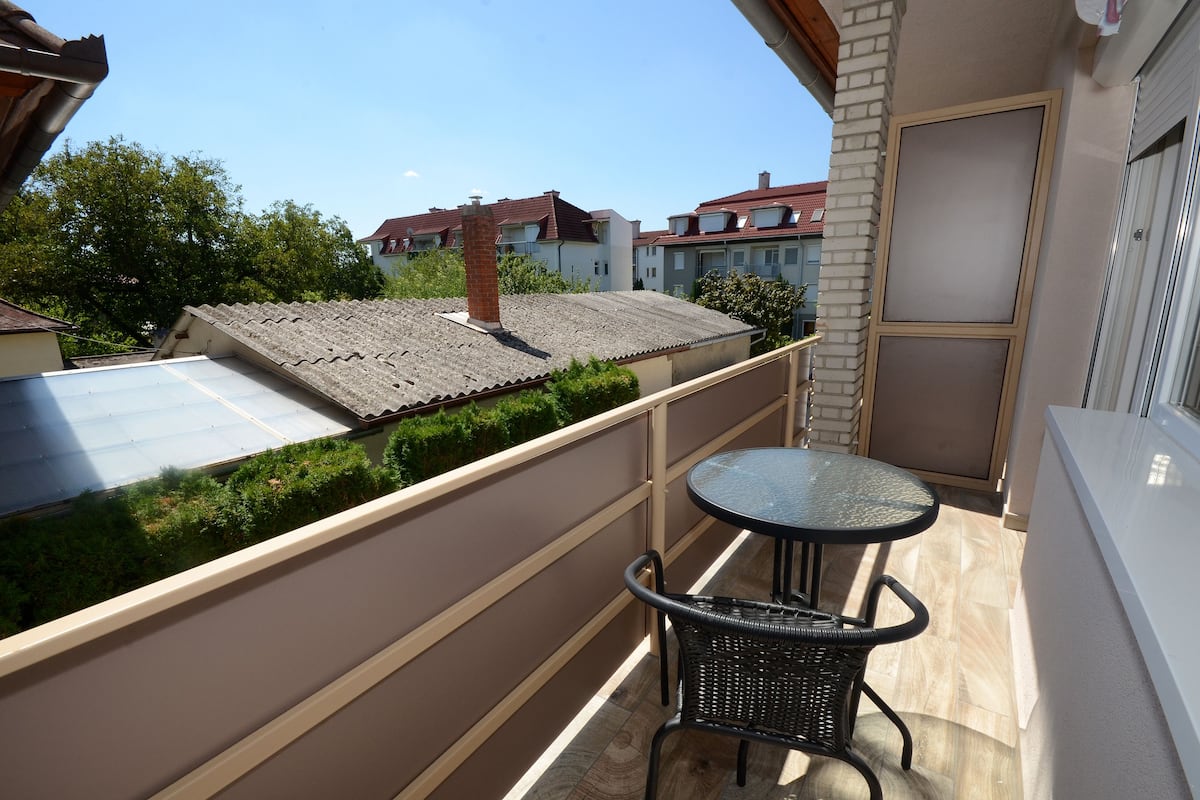 Varanda com mesa e cadeira, vista para casas vizinhas e um muro de tijolos.