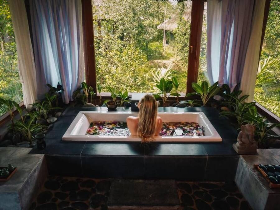 A woman sitting in a bathtub with a view of lush greenery outside.