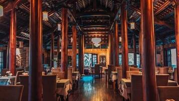 A restaurant with a central open space, wooden pillars, and tables arranged on either side.