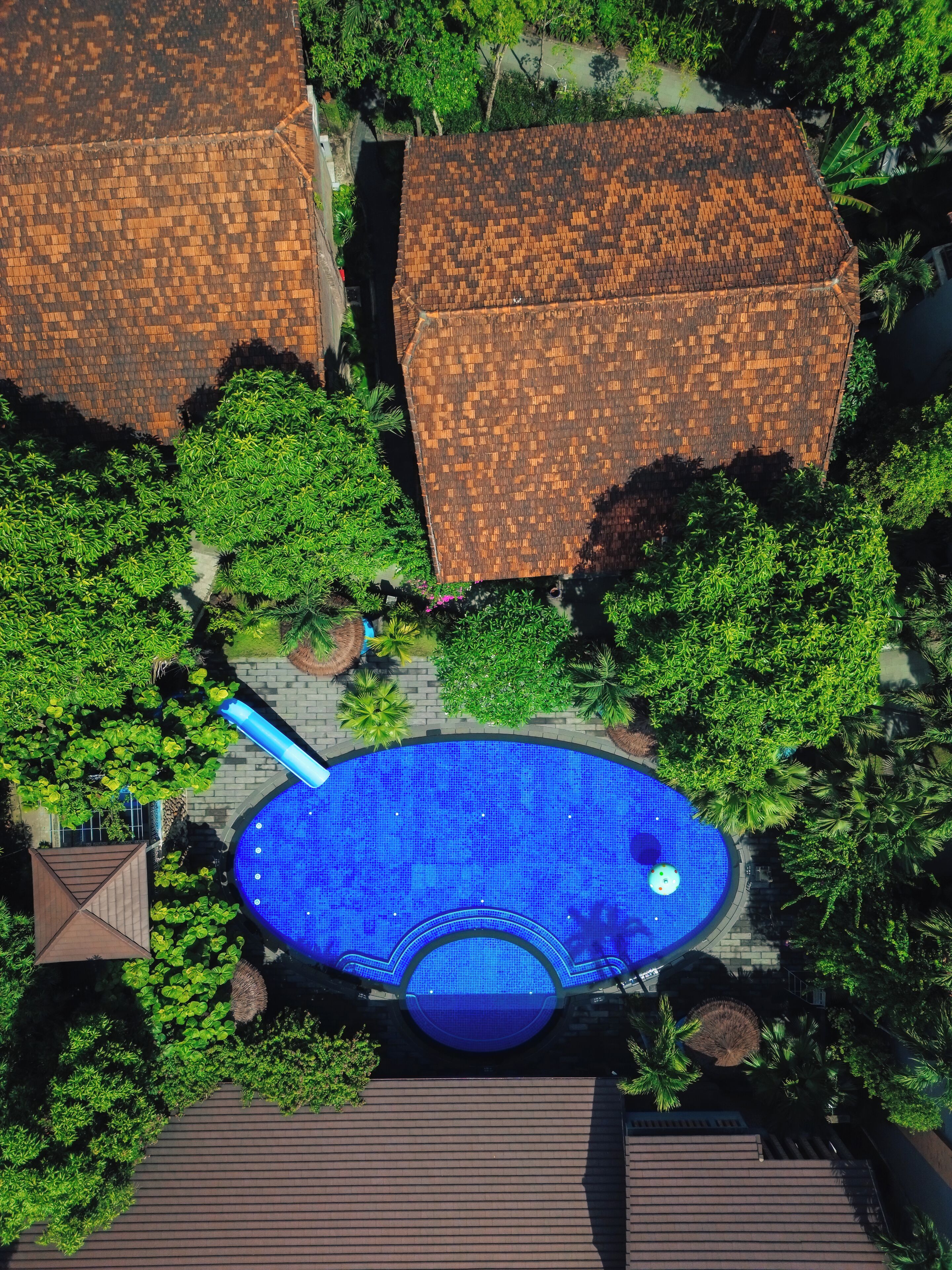 An aerial view of a residential area with a swimming pool surrounded by lush greenery and houses with tiled roofs.