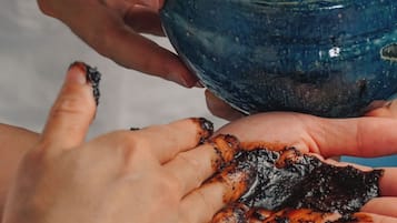 A person holding a blue bowl with a dark substance, another person with a hand covered in the substance, and a third person with a bracelet.