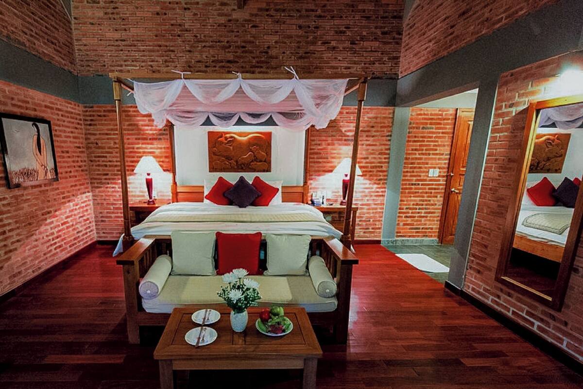 A room with a brick wall, a bed with a canopy, a sofa, a table with plates and a vase, and a mirror on the wall.