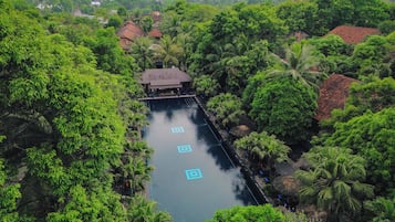 Ein langer Pool mit einer Brücke, umgeben von üppiger Vegetation und traditioneller Architektur.