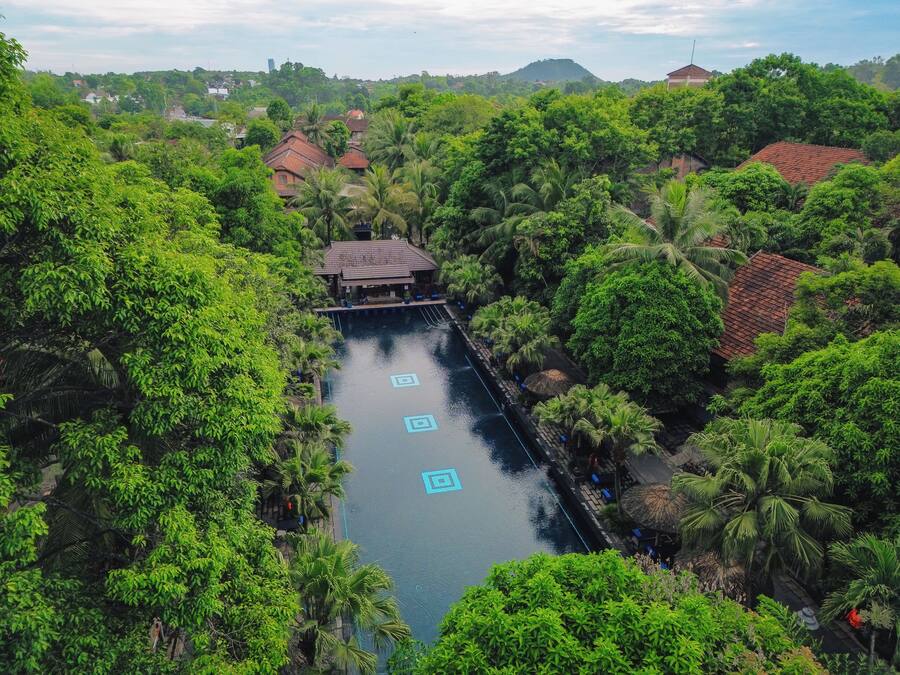 Ein langer Pool mit einer Brücke, umgeben von üppiger Vegetation und traditioneller Architektur.