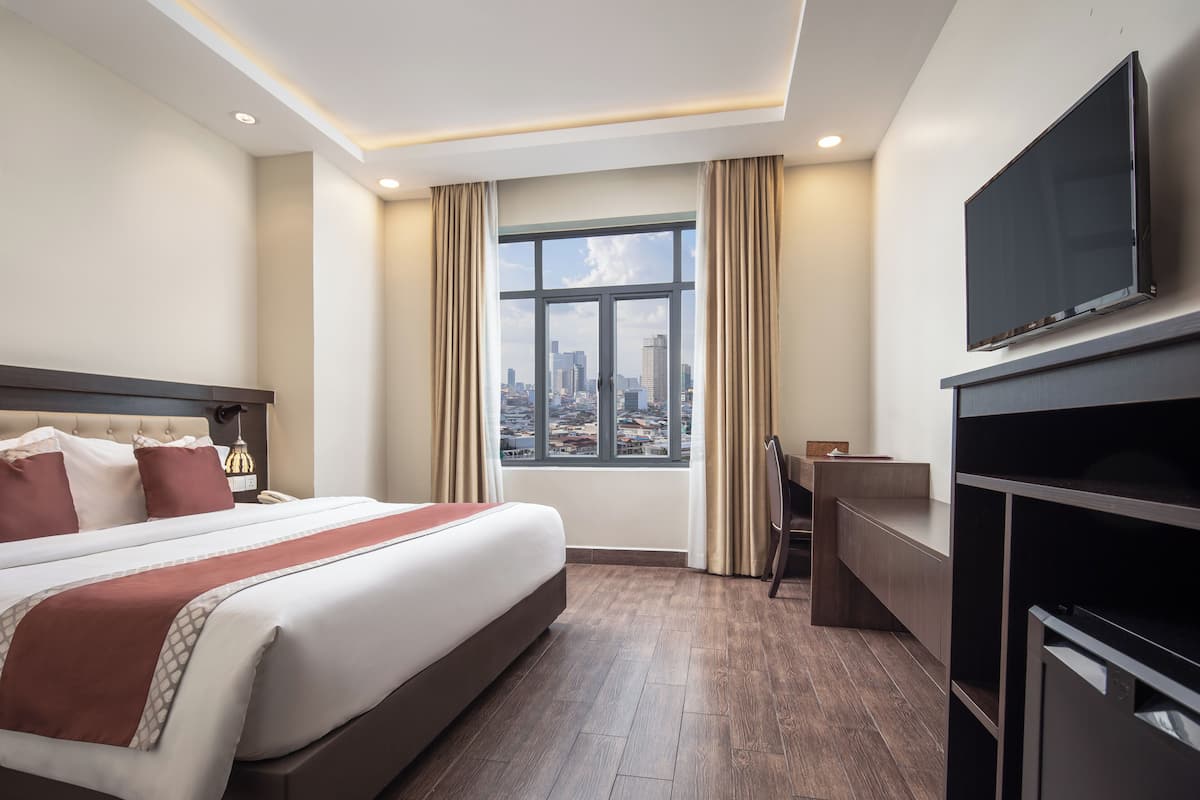 Ein Hotelzimmer mit einem großen Bett, einem Schreibtisch, einem Fernseher und einem Fenster mit Blick auf die Stadt.
