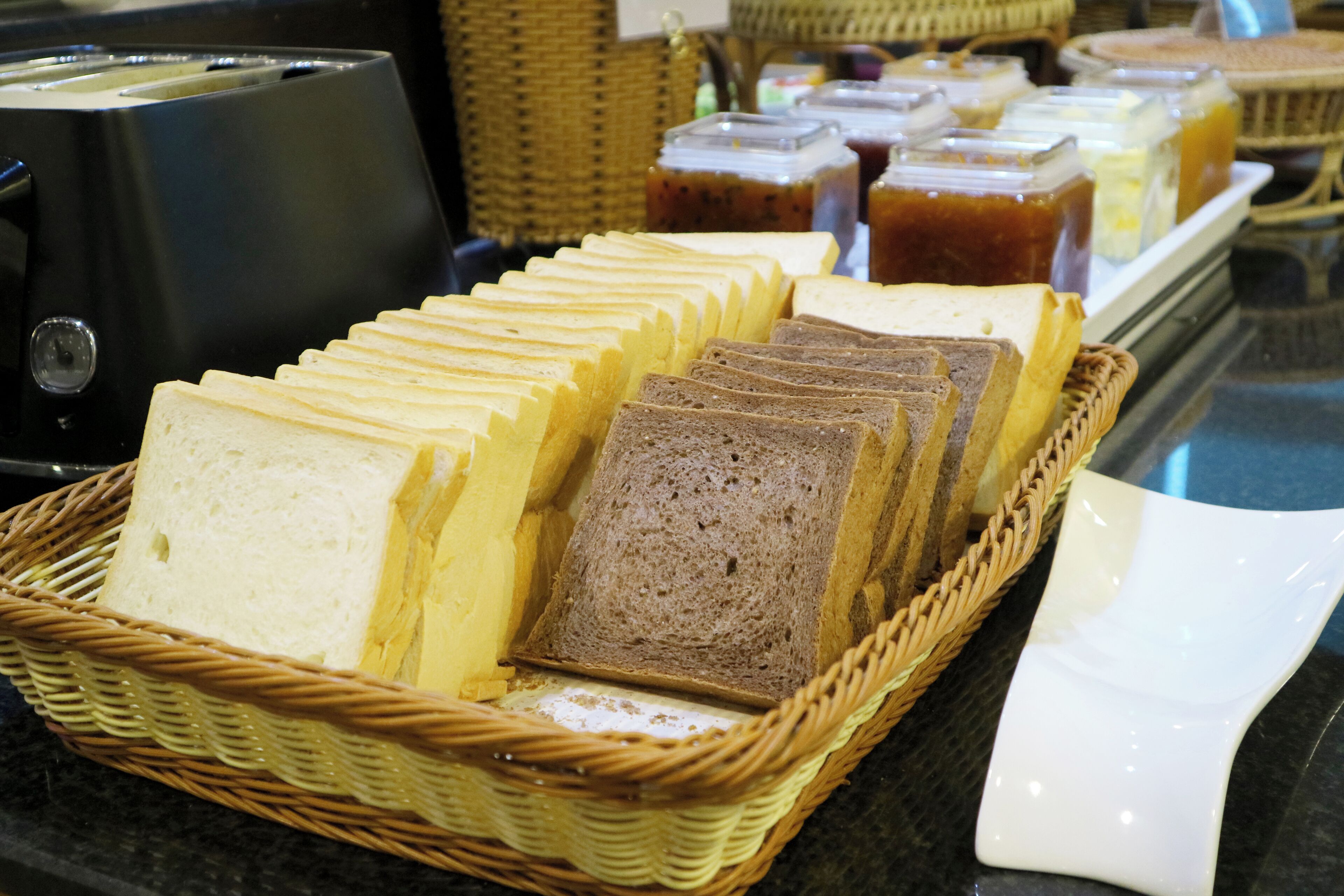 A display of sliced bread in a wicker basket, with various condiments in the background.