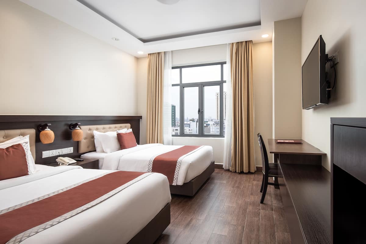 Ein Hotelzimmer mit zwei Betten, einem Schreibtisch, einem Sessel, einem Fernseher und einem Fenster mit Vorhängen.