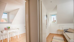 A modern, well-lit room with a dining area, a bed, and a view of a tower through a window. - Top floor apartment (Trogir)
