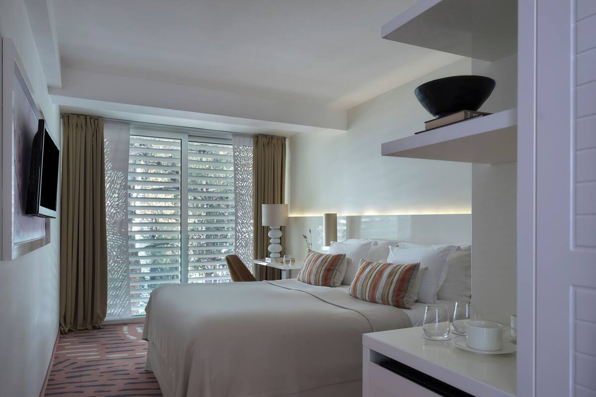 Een hotelkamer met een bed, nachtkastje, lamp en een aan de muur bevestigde televisie.