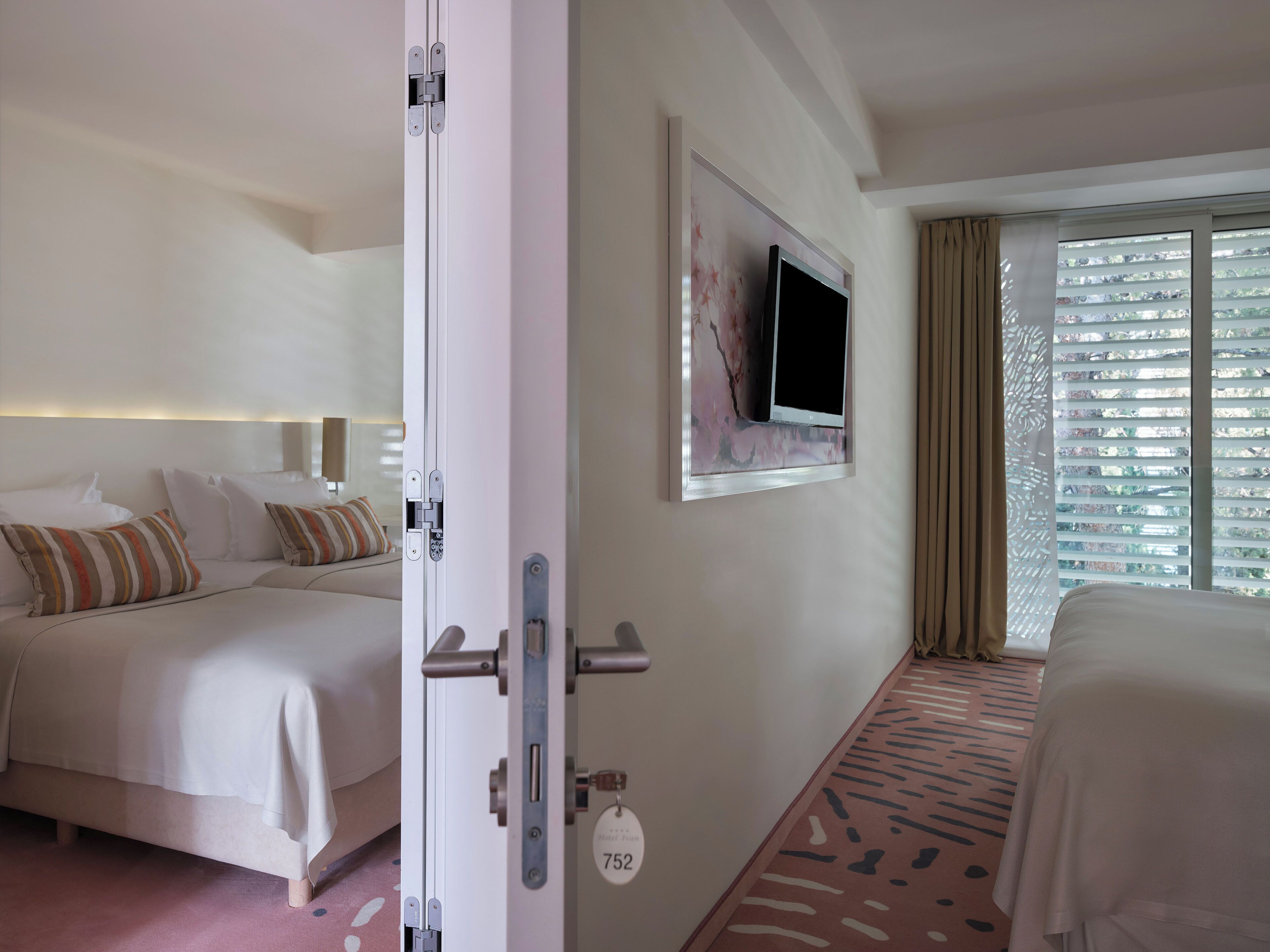 A hotel room with a bed, a television mounted on the wall, and a window with curtains.