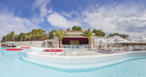 Una gran piscina al aire libre con varias pistas de natación, una zona de estar cubierta y sombrillas para protegerse del sol.