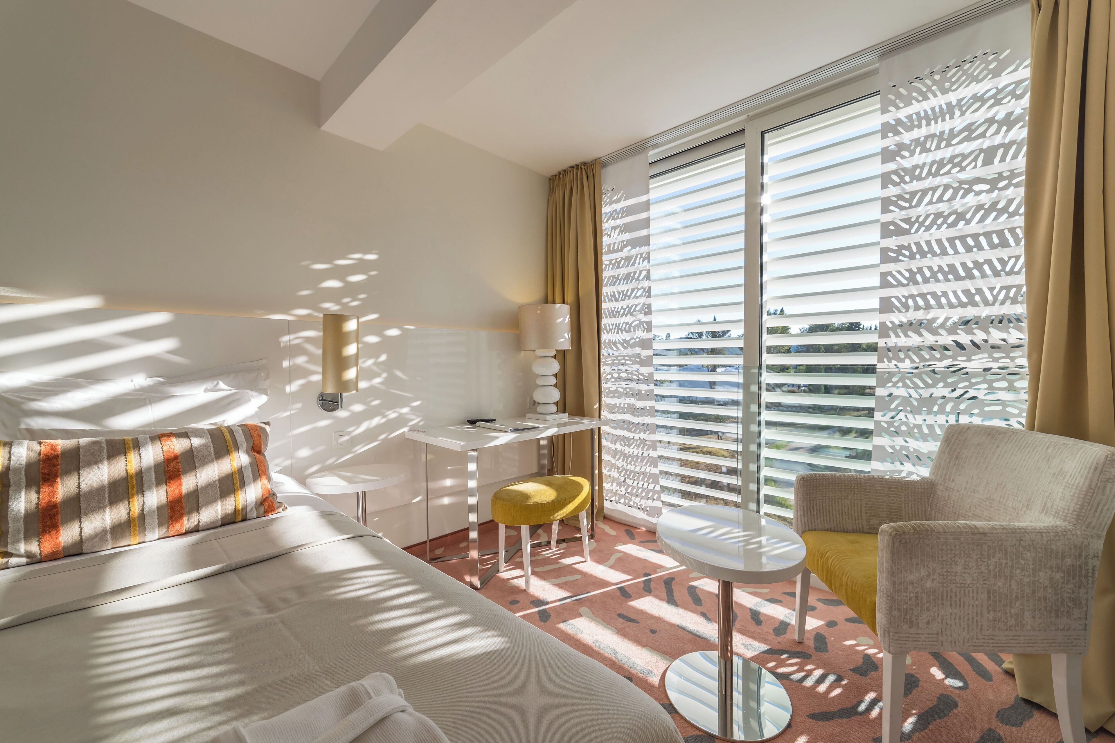 A hotel room with a bed, a desk, a chair, and a window with blinds.