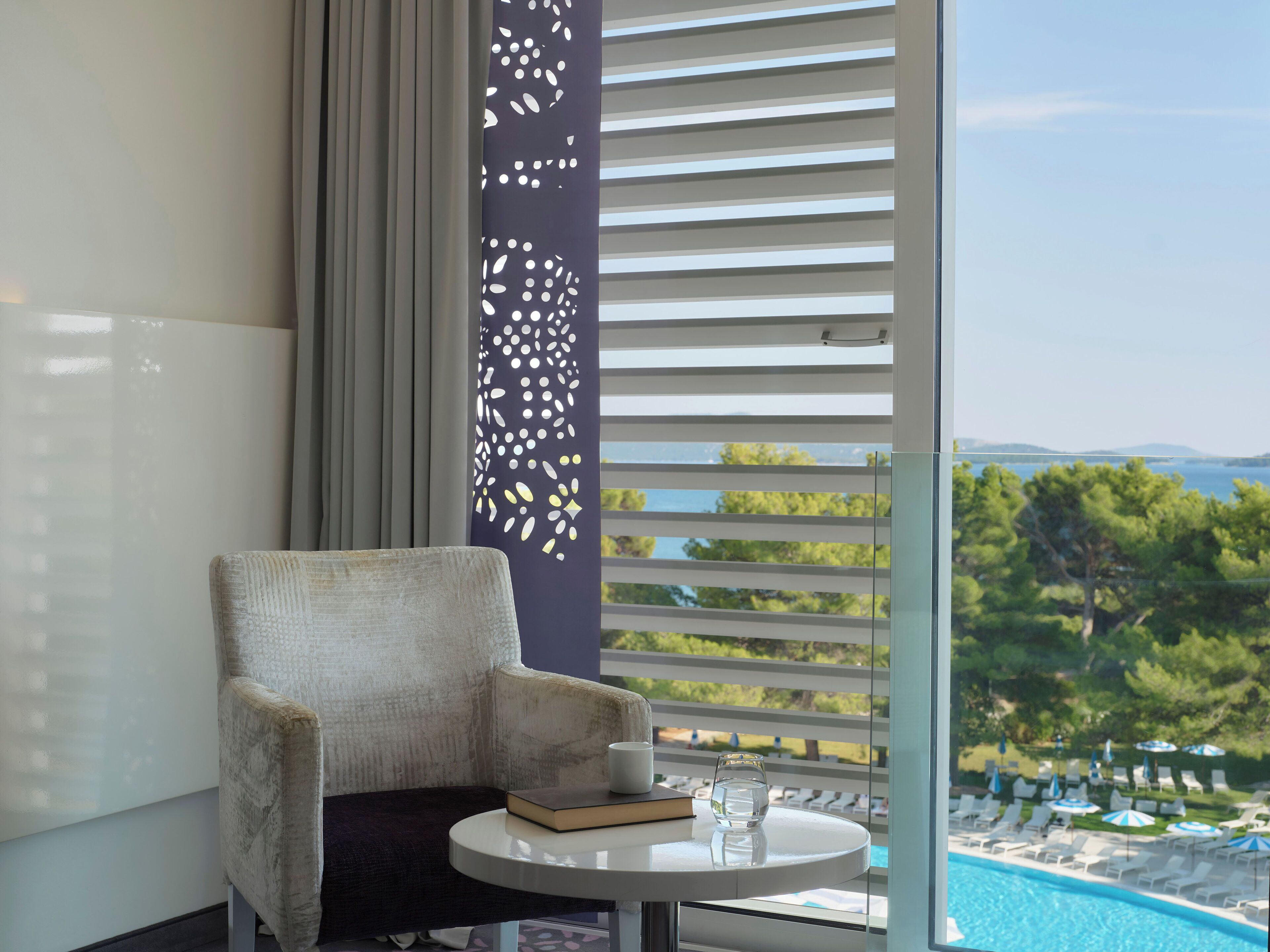 A room with a view of a pool, a chair, a table, and a decorative panel.