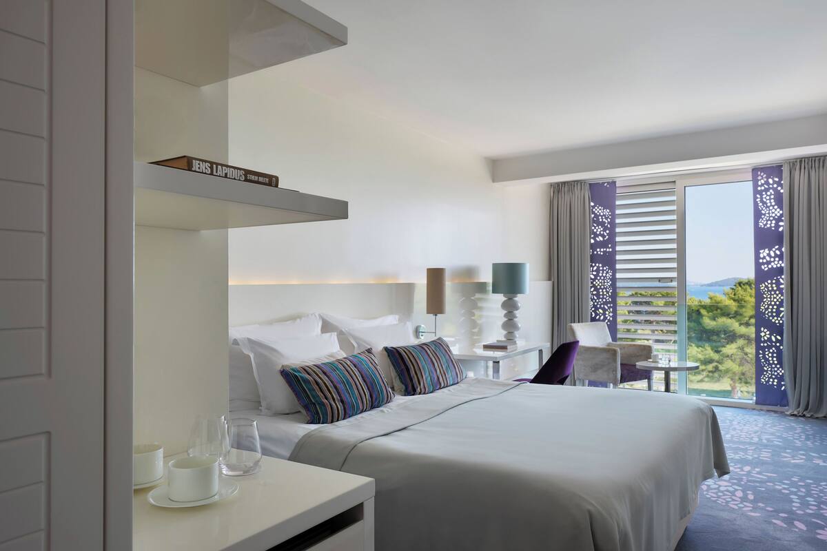 Een hotelkamer met een bed, nachtkastjes, een stoel en uitzicht op de omgeving.