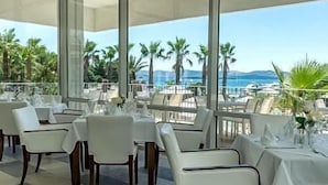 An outdoor dining area with tables and chairs, overlooking a scenic view of palm trees and the sea.