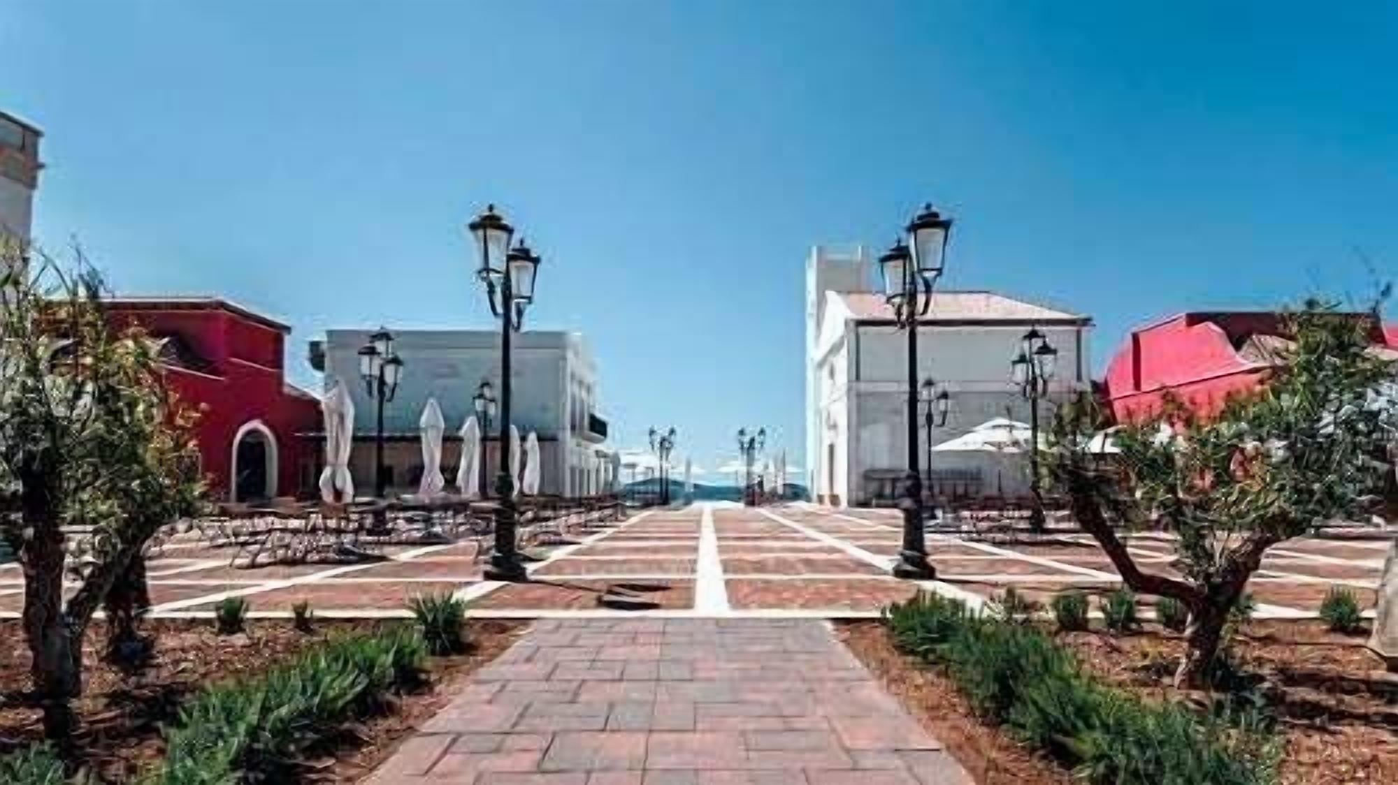 A paved pathway leading to a building with a red facade and a white building in the background.