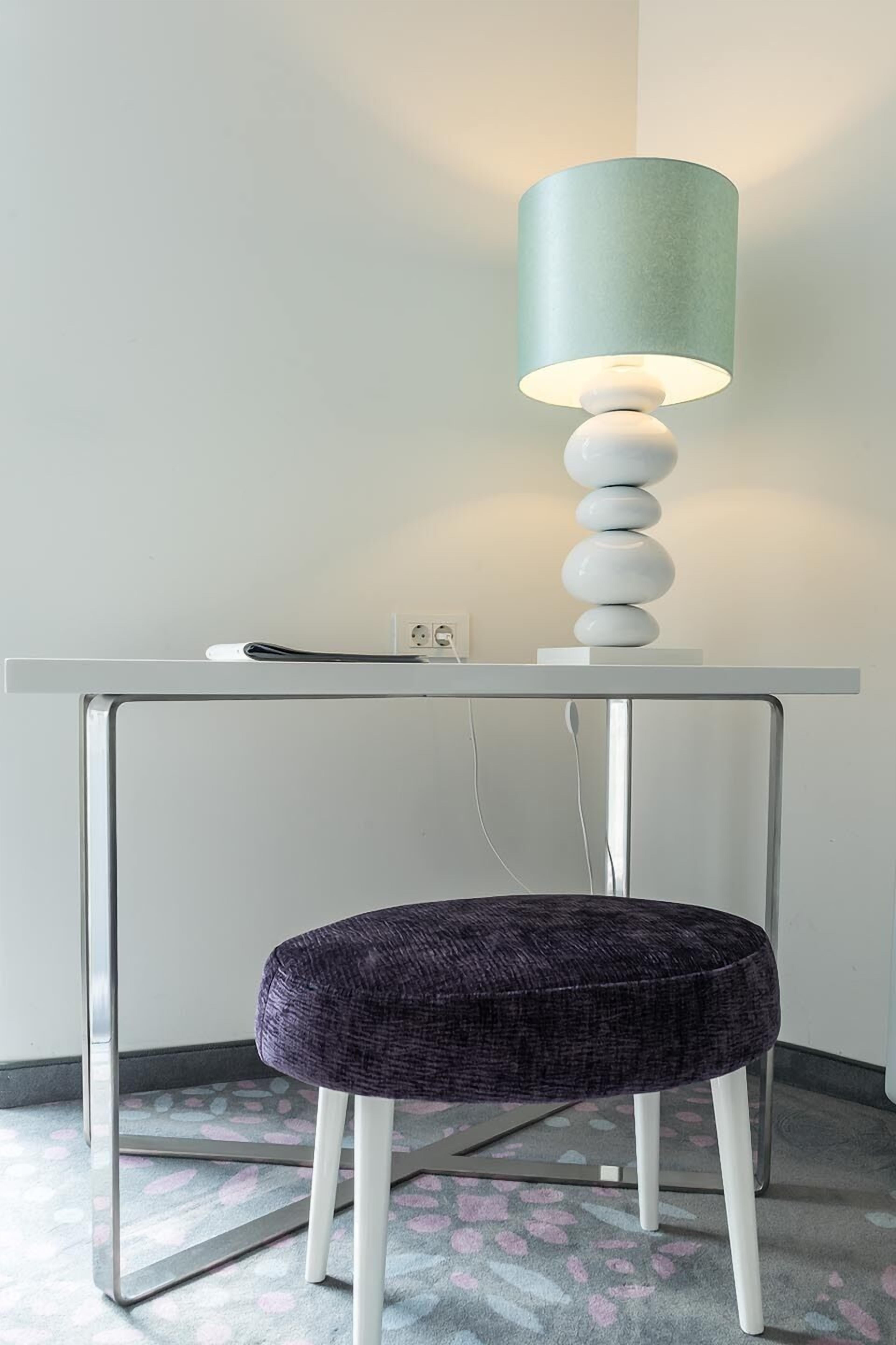 A modern desk with a lamp, a power outlet, and a patterned rug.