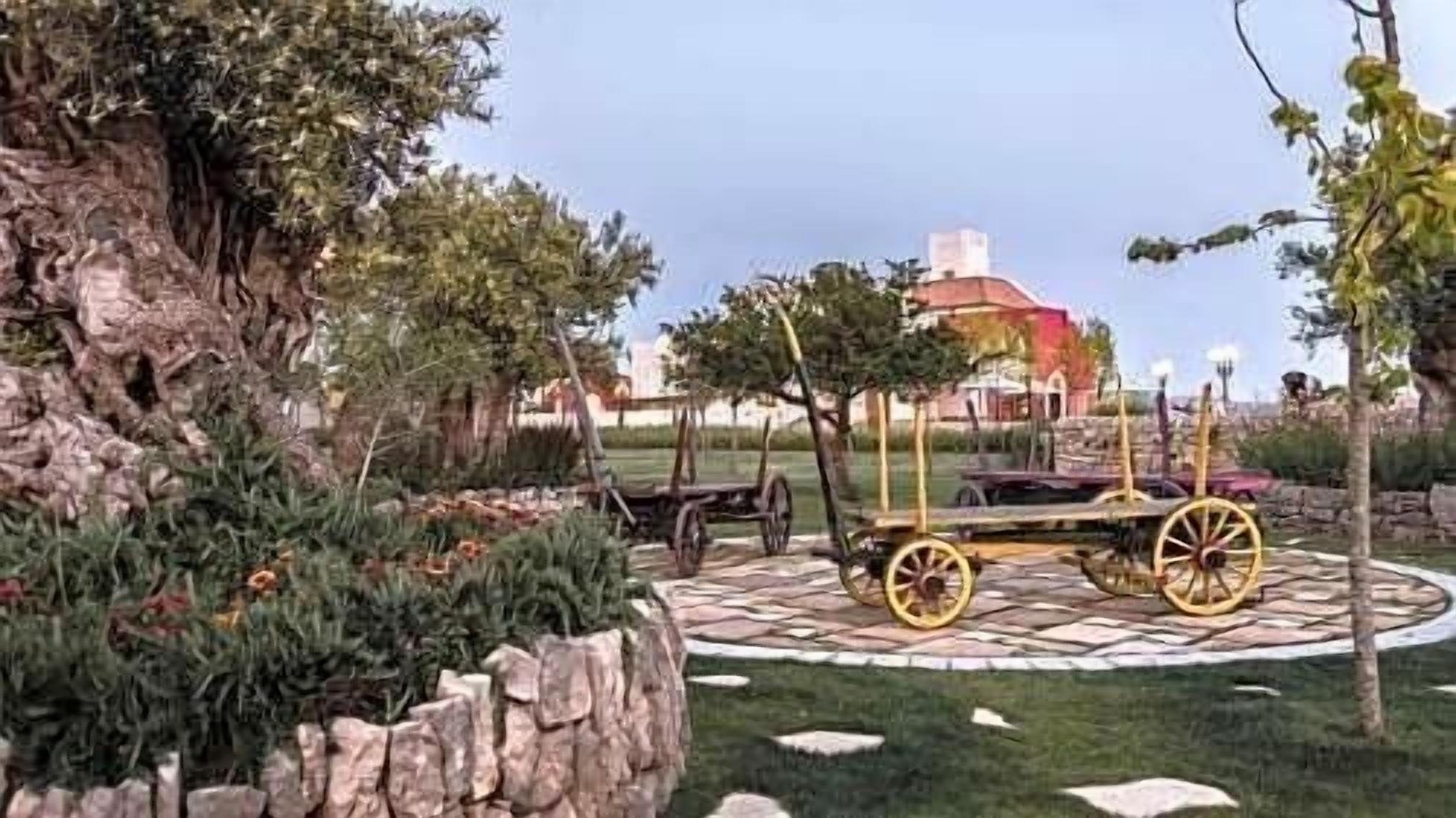 A garden with a stone pathway, a wooden cart, and a building with a red roof in the background.