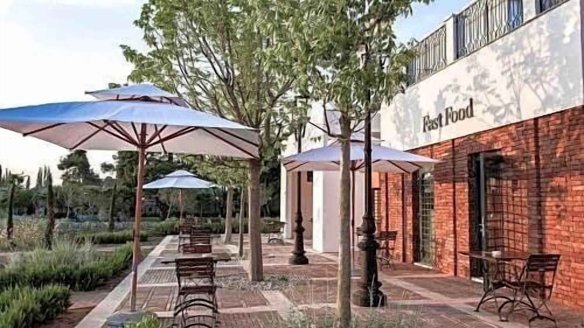 An outdoor patio area with tables and chairs, umbrellas, and a brick building with a sign that reads "Fast Food."