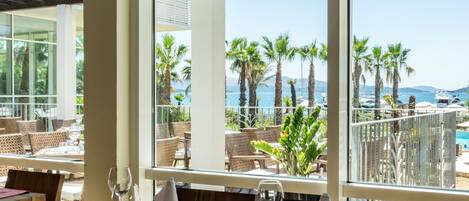 A restaurant with a view of the sea and palm trees.