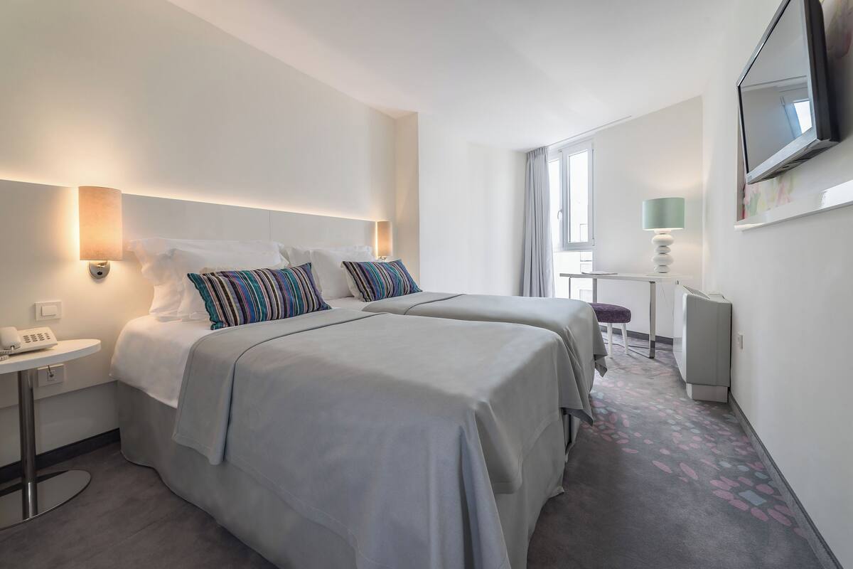 Hotelkamer met twee bedden, een bureau, telefoon, televisie en een raam met gordijnen.