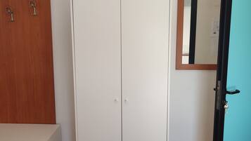 Ein Zimmer mit einem weißen Schrank, einer hölzernen Bank und einer Tür mit Spiegel.