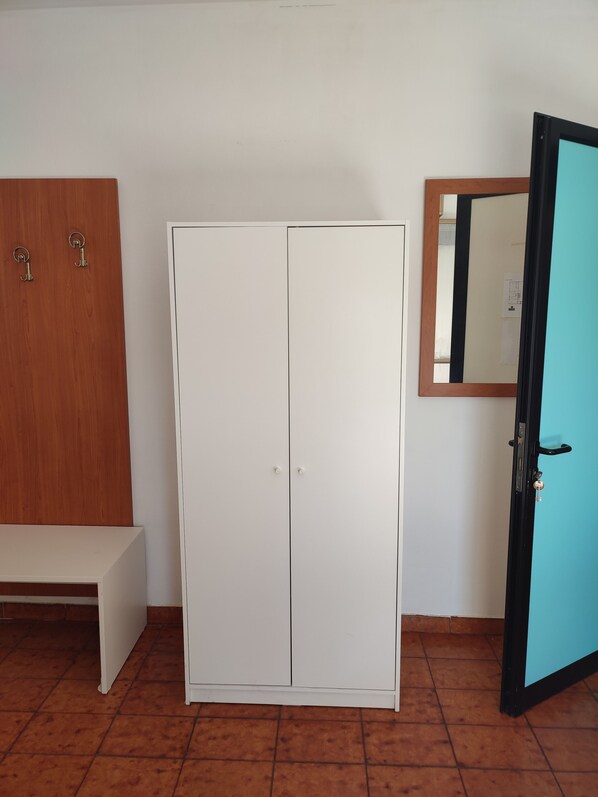 A room with a white wardrobe, a wooden bench, and a door with a mirror.