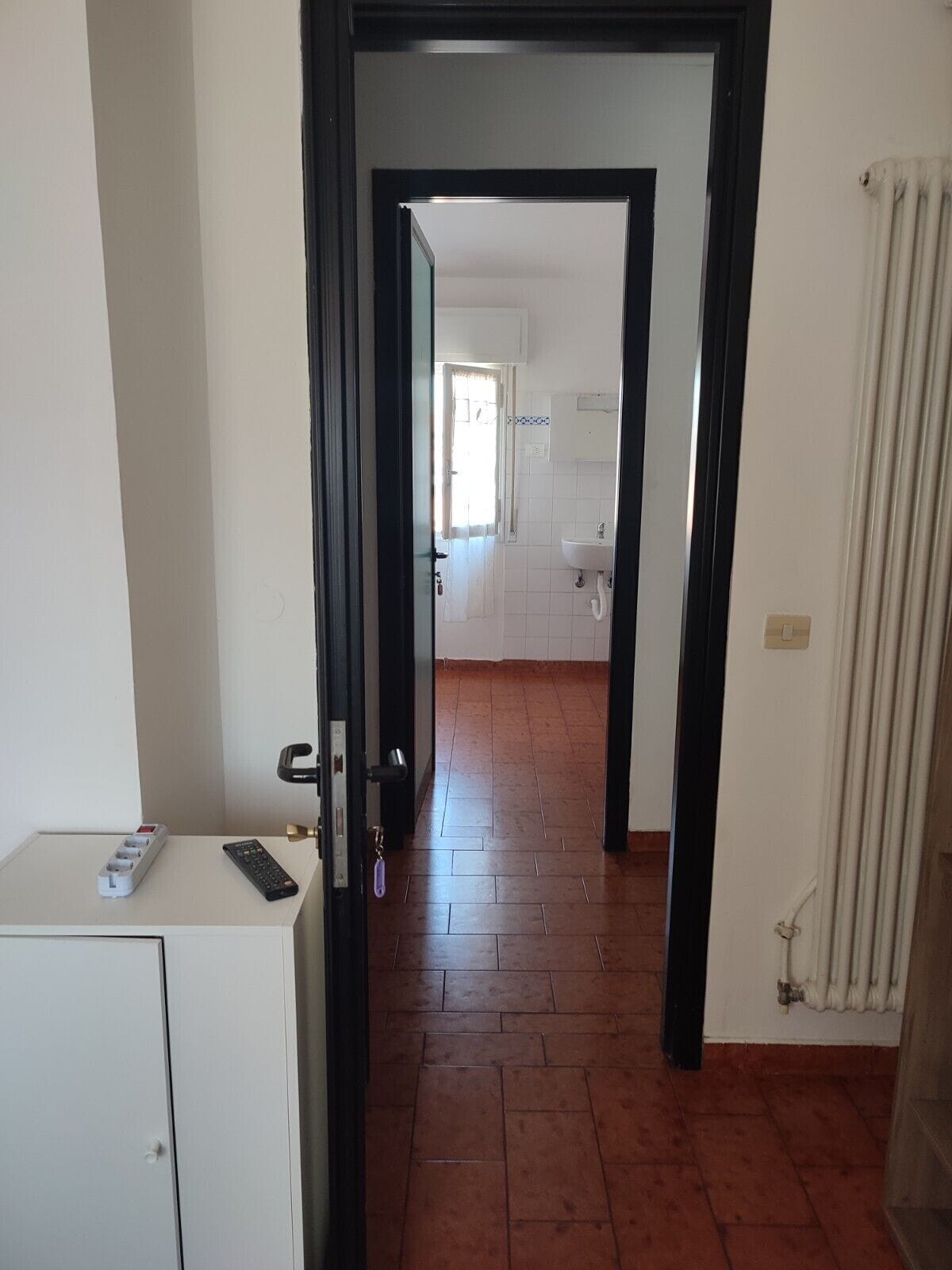 Un pasillo que conduce a un baño con un lavamanos blanco y piso de baldosas.