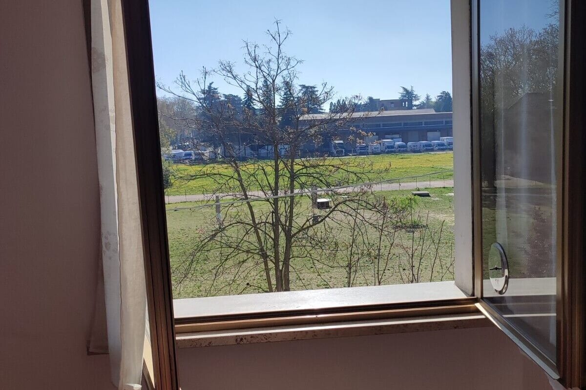 A room with a large window overlooking a grassy area and a building in the distance.