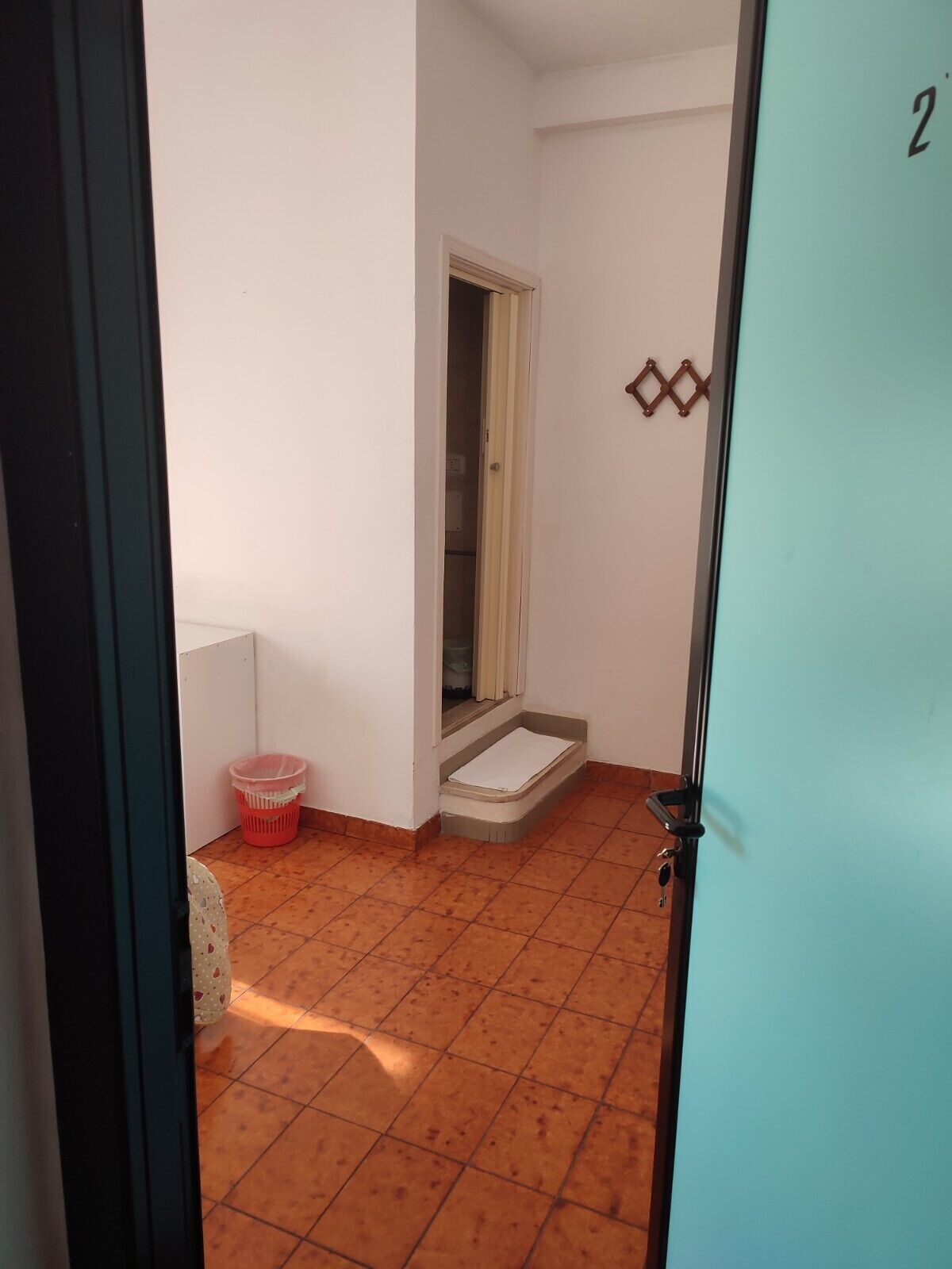 A narrow hallway with a tiled floor, a door with a number, and a small step leading to a room.