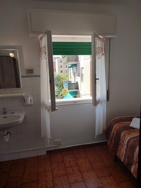 A small, clean room with a bathroom, a bed, and a window with curtains. - Albergo Italia (Reggio nell'Emilia)