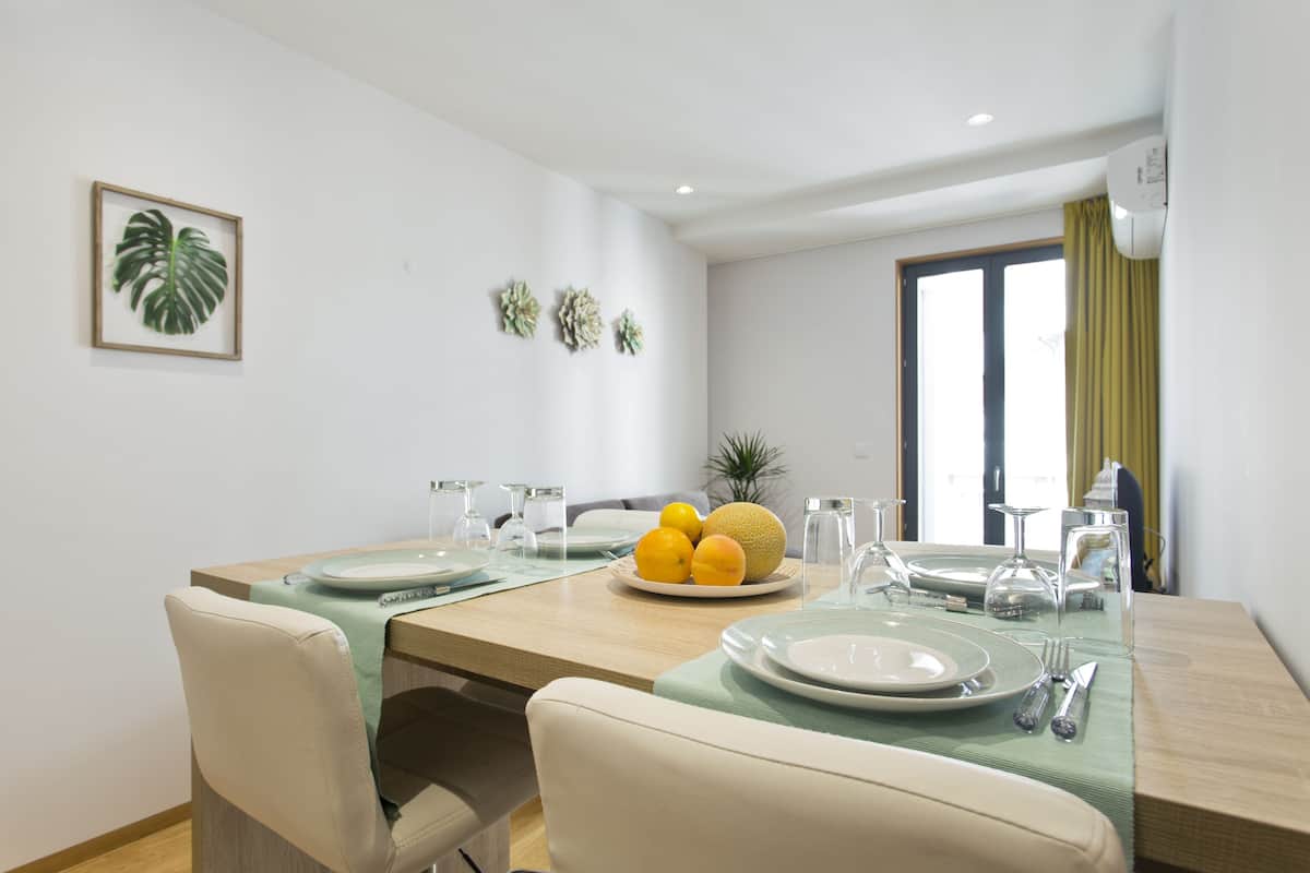 A dining area with a wooden table set for four, including plates, cutlery, and a fruit bowl.