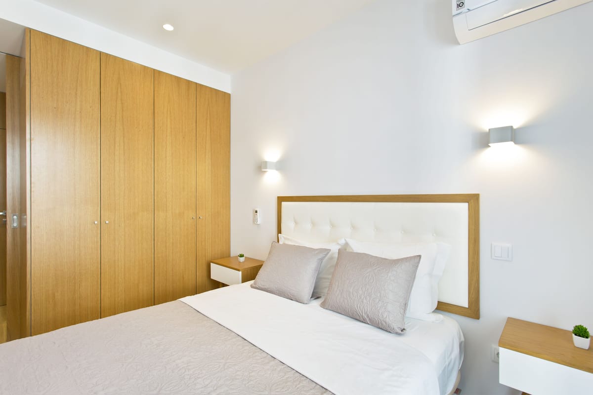 A bedroom with a large wooden wardrobe, a bed with white bedding, two bedside tables, and wall-mounted lighting.