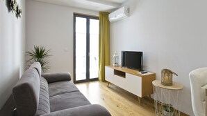 Una sala de estar moderna con un sofá gris, un mueble de madera con un televisor, una mesita auxiliar y una planta en maceta.