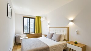 Habitación de hotel con una cama grande, una mesita de noche, una silla, una ventana con cortinas y un aire acondicionado de pared.
