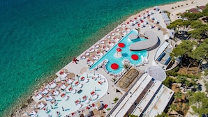 An aerial view of a resort with a large pool area, multiple lounge chairs, and a beach.