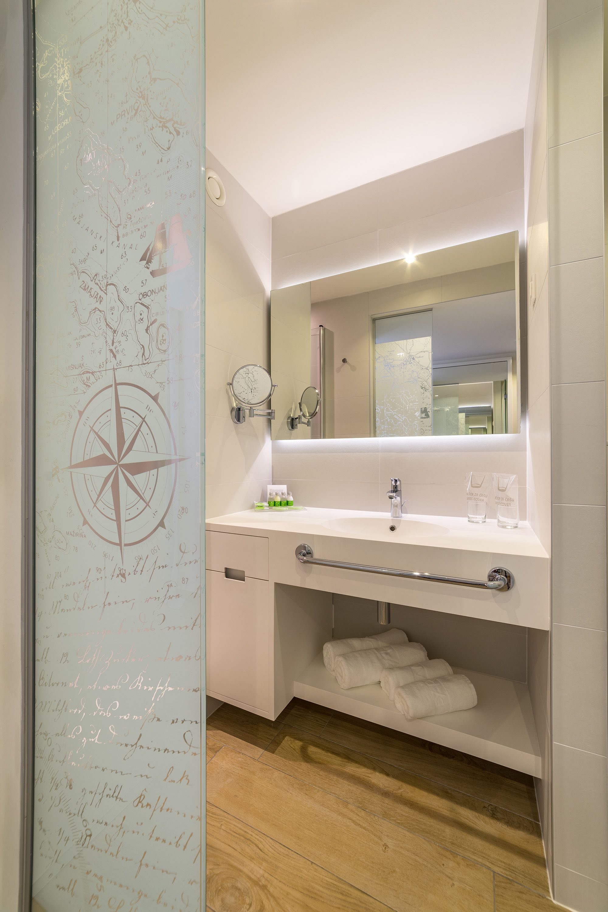 Une salle de bain moderne avec un grand miroir, un lavabo blanc et un plancher en bois.