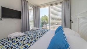 A hotel room with a bed, a TV, and a window with blinds.