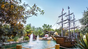 A pirate ship docked by a calm water body with a fountain in the background.