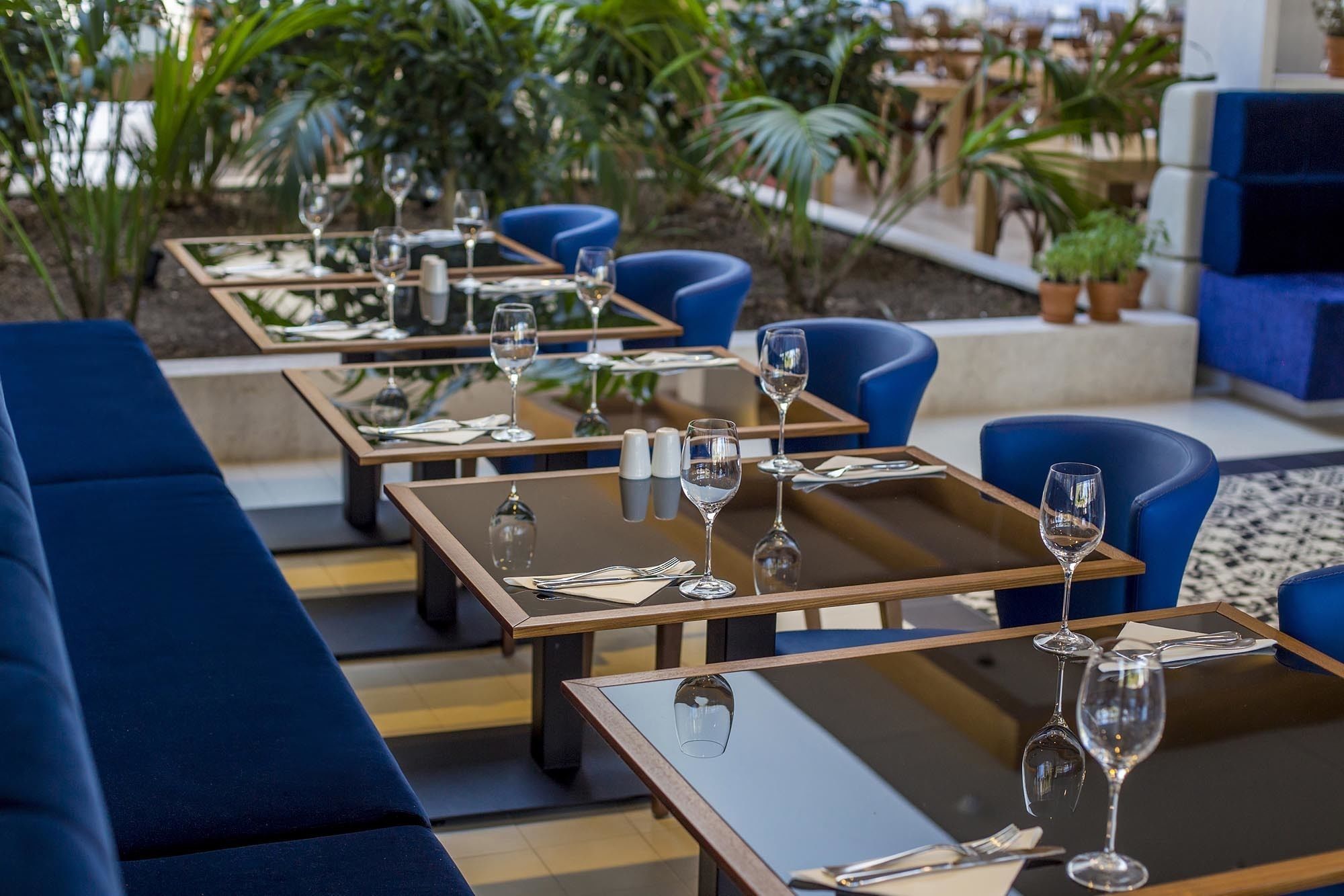 A restaurant with tables set for dining, blue chairs, and a view of the outdoors.