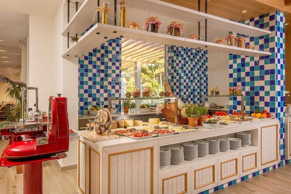Ein reichhaltiges Buffet mit verschiedenen Speisen, einem roten Gerät und einer Wand mit blau-weißen Schachfeldern.