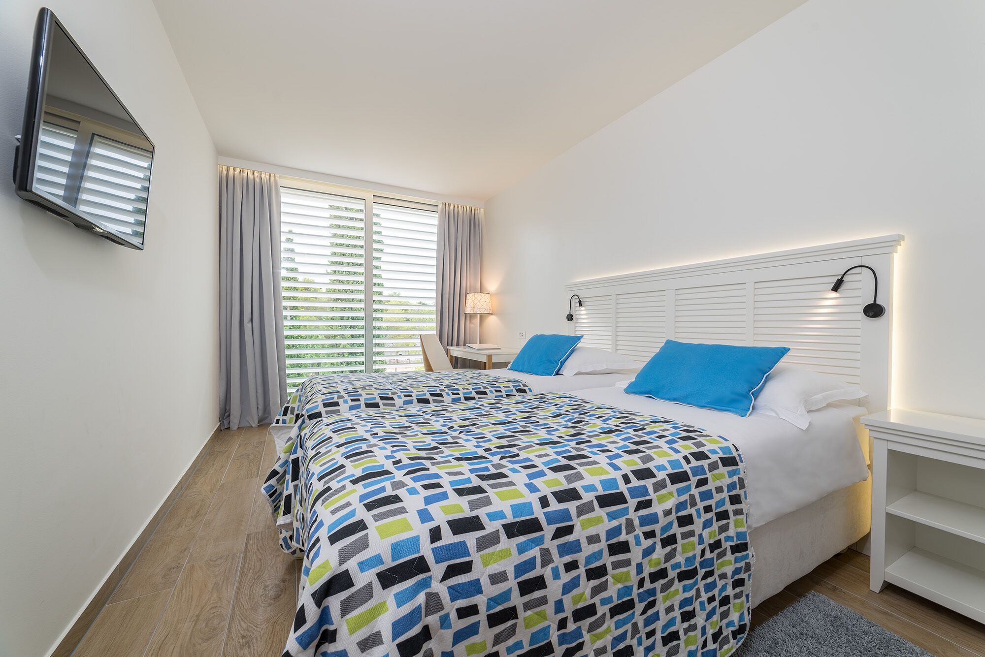 Ein Hotelzimmer mit einem großen Bett, einem Nachttisch, einer Lampe und einem an der Wand befestigten Fernseher.