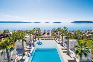 Zona de piscina con sillones reclinables y palmeras, con vista a una masa de agua y islas distantes.